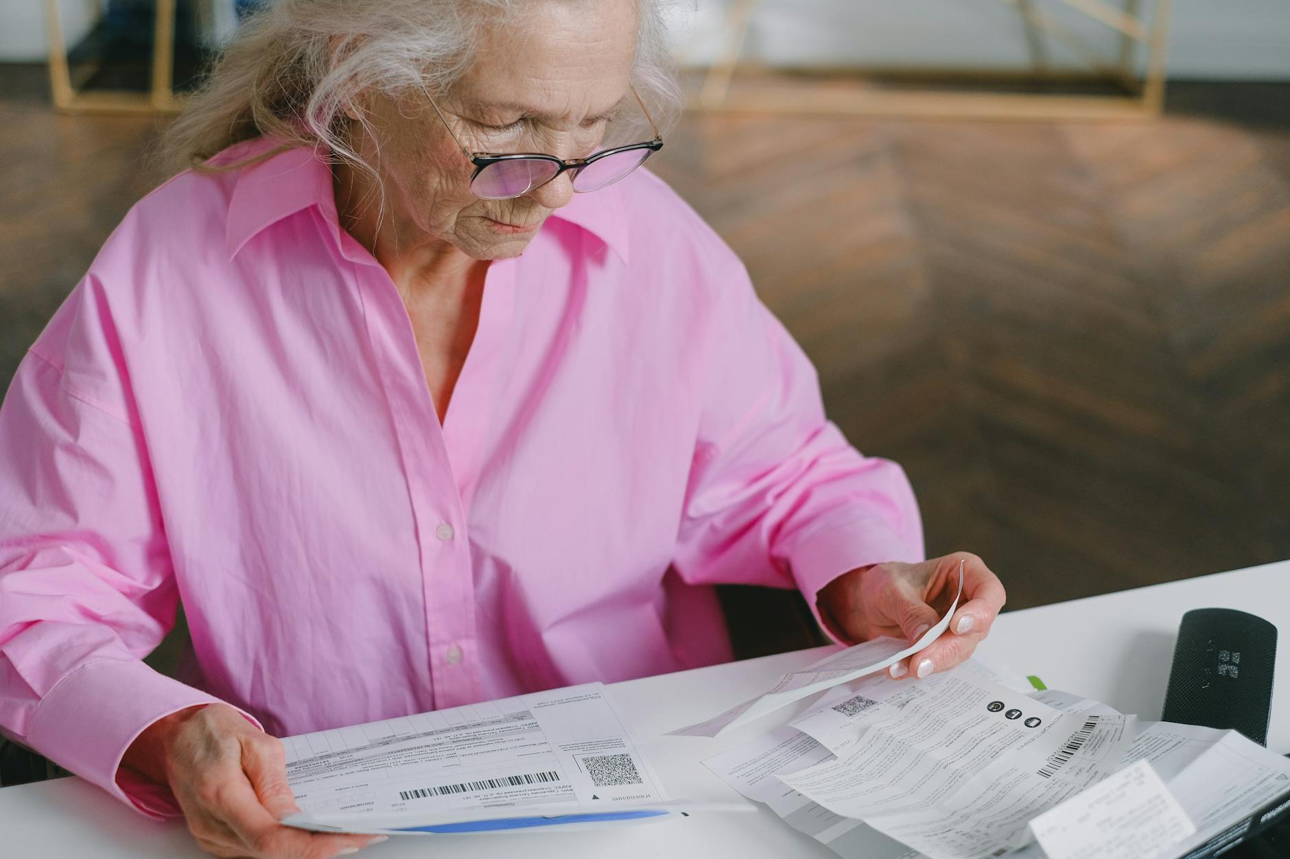 an elderly woman in pink long sleeves sitting while reading documents
