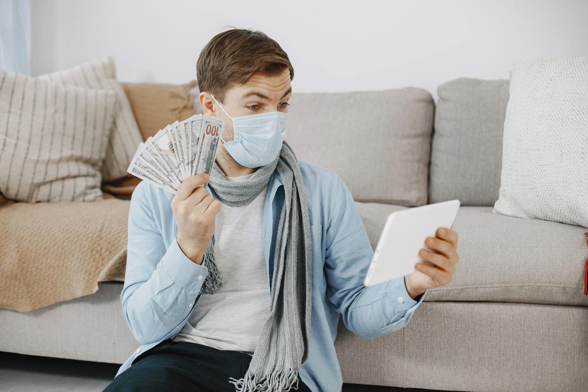 man wearing a face mask at home on a video call and showing money