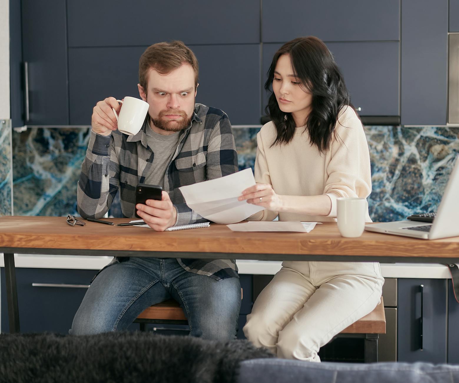 a man looking at the paper while holding a coffee and phone