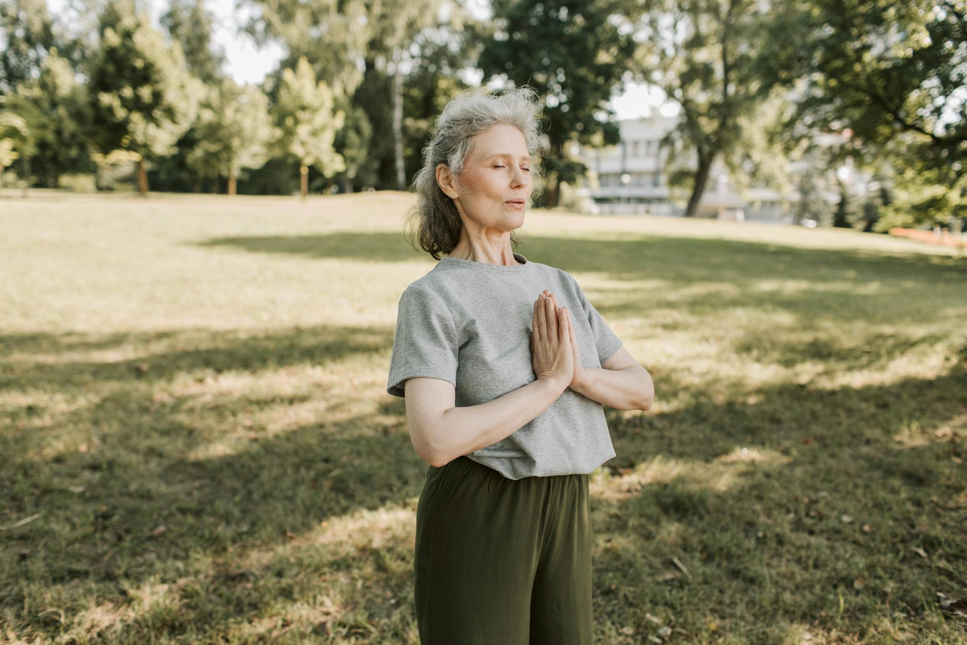 an elderly woman in gray shirt meditating at the park