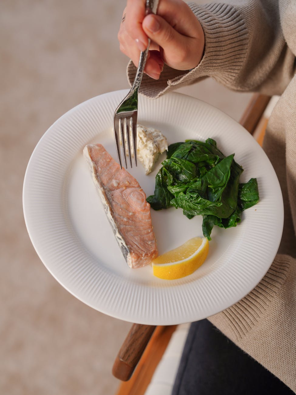 close up of woman holding a plate with fish spinach and lemon