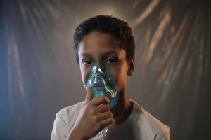a boy in white shirt holding green oxygen mask