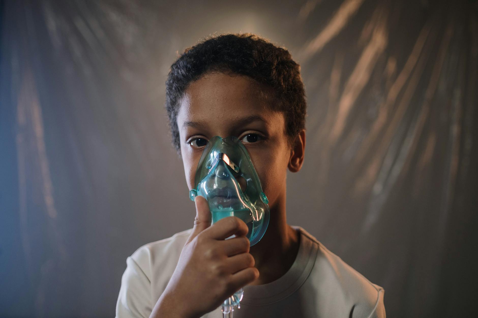 a boy in white shirt holding green oxygen mask